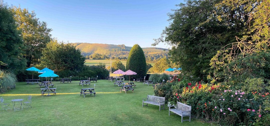 The Three Horseshoes beer garden with picnic tables and colourful parasols overlooking the South Downs countryside in Elsted, Sussex