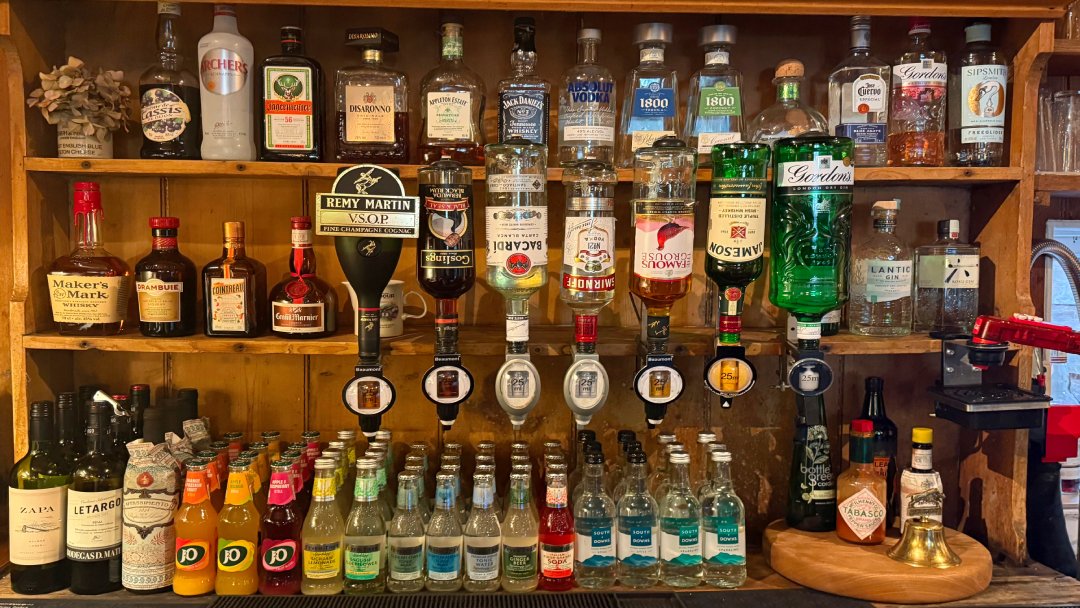 Back bar at The Three Horseshoes in Elsted, with spirits on wooden shelves, optics and bottled mixers